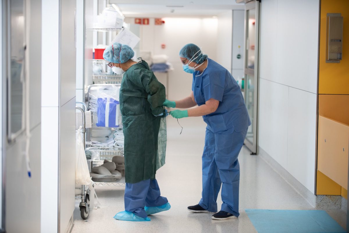 Una professional sanitària corda a una companya una bata abans d'atendre un pacient amb covid-19. Foto: ACN.