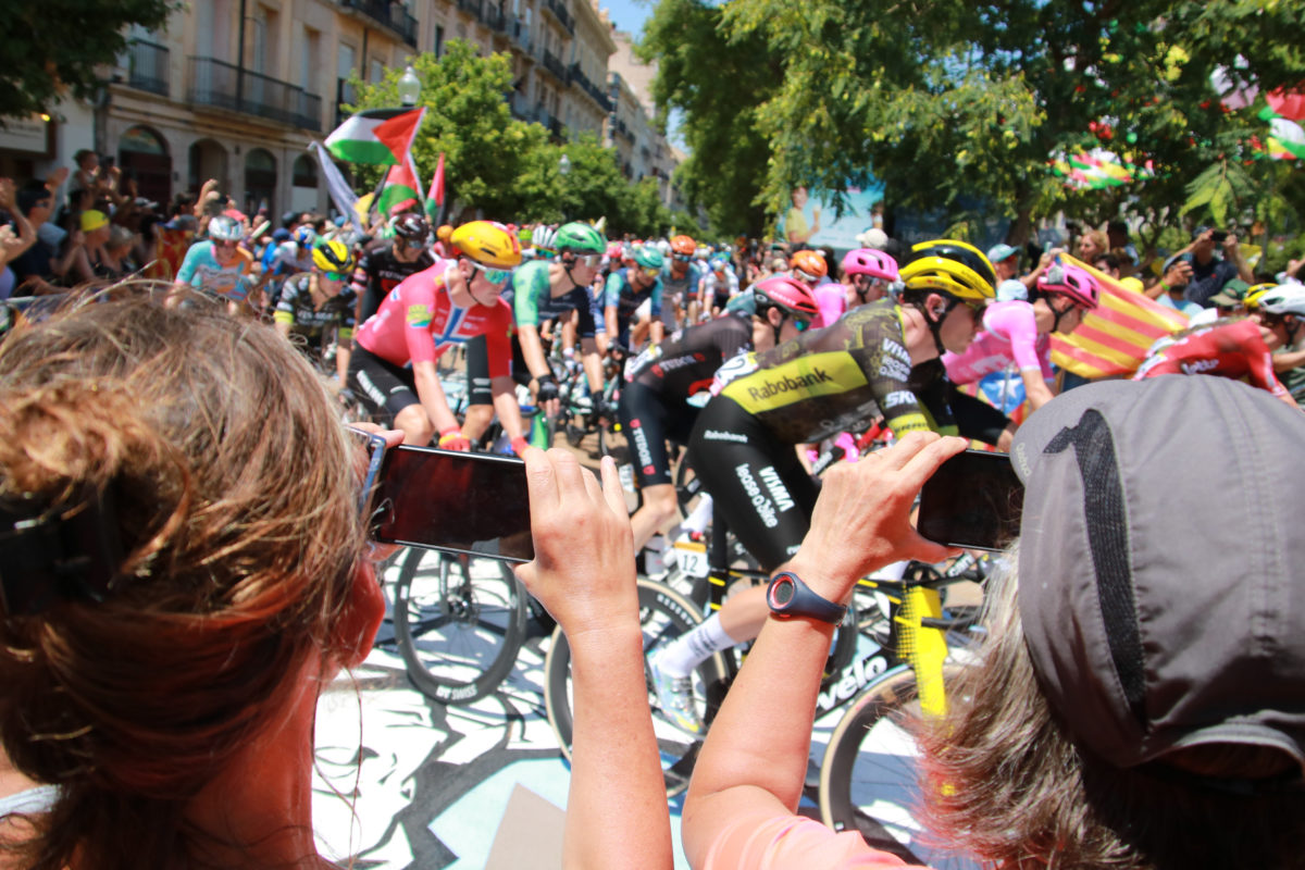Dues dones fotografien el gran grup del Tour de França, al seu pas per la Rambla Nova de Tarragona. Data de publicació: diumenge 05 de juliol del 2026, 14:51 Localització: Tarragona Autor: Ariadna Escoda/Mar Rovira