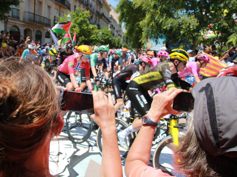 Dues dones fotografien el gran grup del Tour de França, al seu pas per la Rambla Nova de Tarragona. Data de publicació: diumenge 05 de juliol del 2026, 14:51 Localització: Tarragona Autor: Ariadna Escoda/Mar Rovira